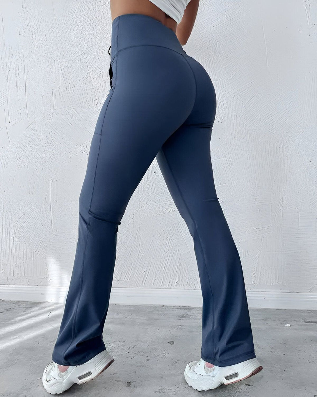 Une femme porte un legging bleu marine taille haute et évasé. Elle est vue de dos et porte des baskets blanches.