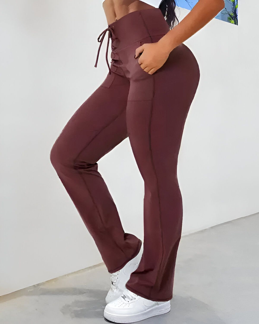 Une femme porte un pantalon de yoga marron taille haute avec un laçage à la taille. Elle est également porte une paire de baskets blanches.