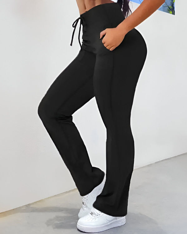 Une femme porte un pantalon de yoga noir moulant taille haute avec un cordon de serrage à la taille et des baskets blanches.