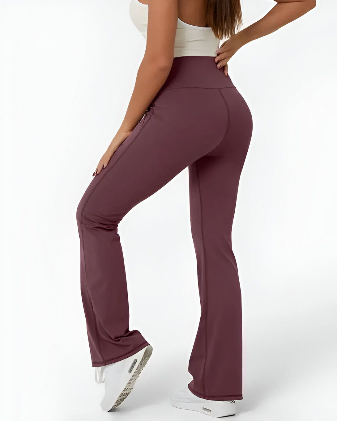 Une femme porte un legging taille haute évasé couleur prune et un débardeur blanc. Elle est vue de dos et porte des baskets blanches.