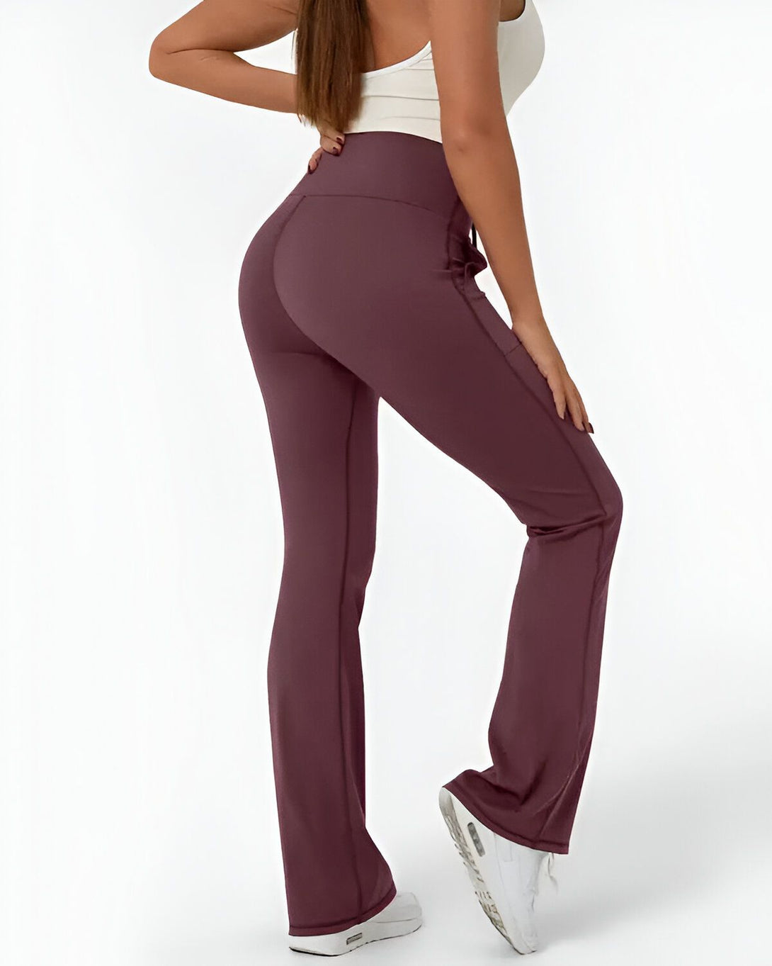 Une femme porte un legging taille haute évasé couleur prune et un débardeur blanc. Elle est vue de dos et porte des baskets blanches.