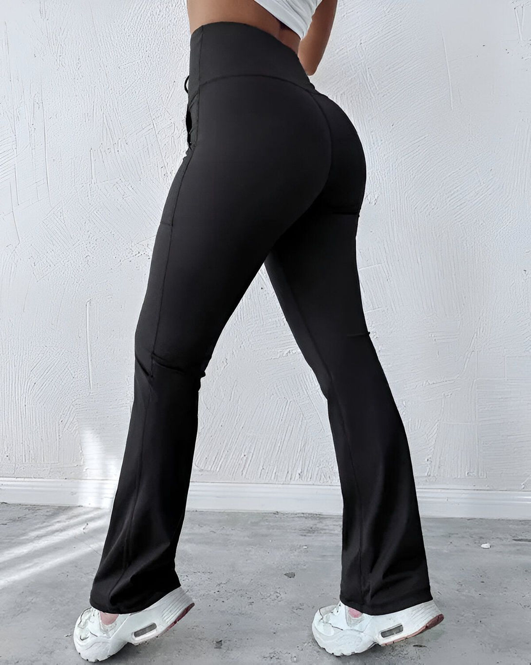Une femme porte un legging noir moulant taille haute avec des baskets blanches.