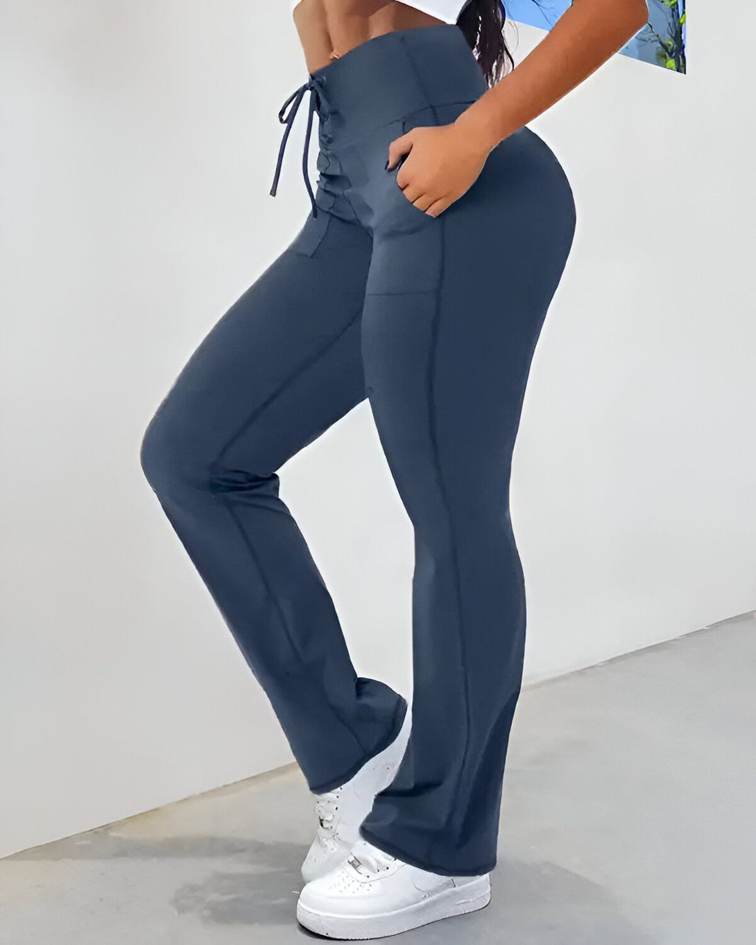 Une femme porte un legging bleu marine taille haute avec un laçage sur le côté. Elle porte également des baskets blanches et une brassière de sport bleue.