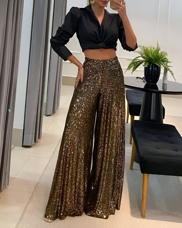 Une femme porte un pantalon large et doré à paillettes avec une chemise noire courte nouée sur le devant.
