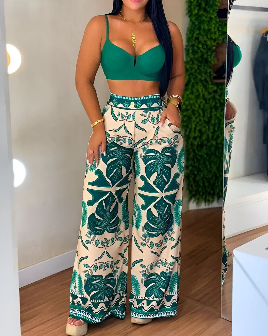 Une femme porte un pantalon taille haute vert et beige à motif de feuilles tropicales. Elle porte également un soutien-gorge vert.