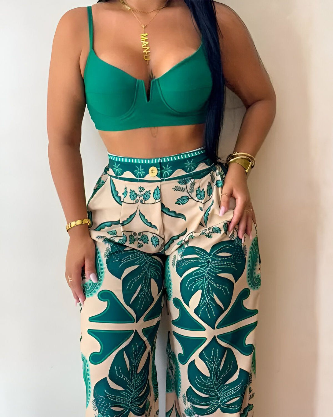 Une femme porte un haut de bikini vert et un pantalon taille haute à motifs de feuilles tropicales. Elle porte également un collier et des bracelets.