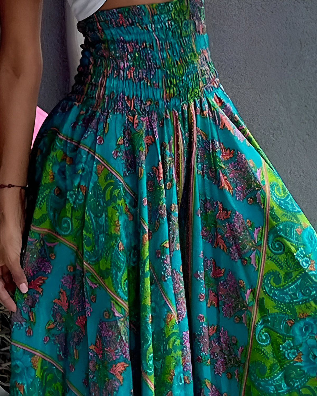 Une femme porte une jupe longue ample à taille haute. La jupe est bleu turquoise à motifs floraux multicolores.