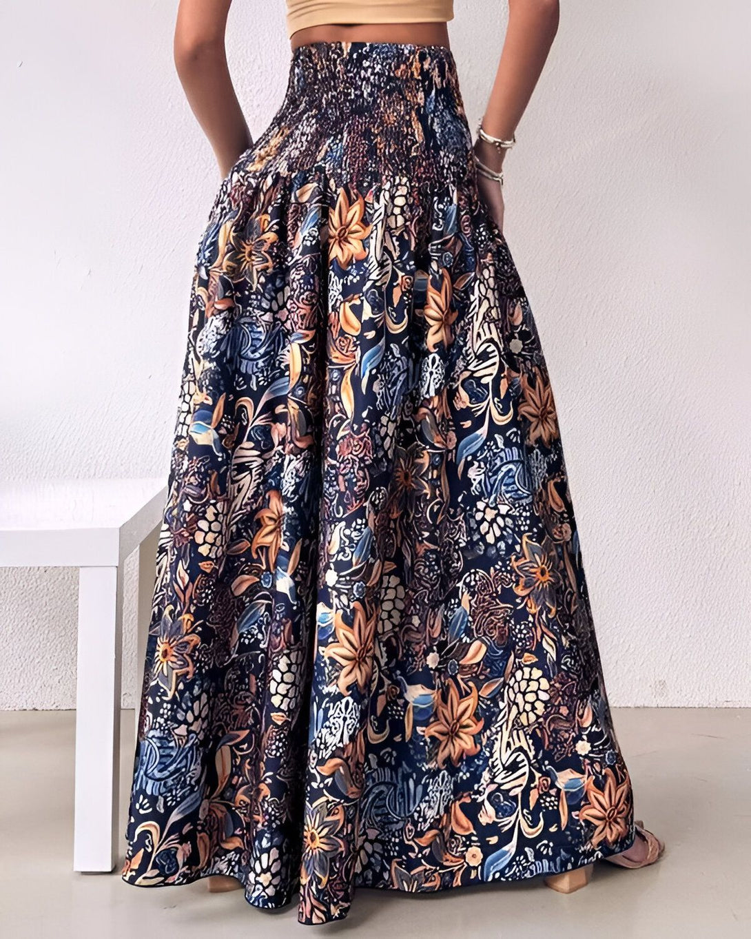Une femme porte une longue jupe ample à taille haute. La jupe est bleu marine avec des motifs floraux multicolores. La femme est vue de dos.