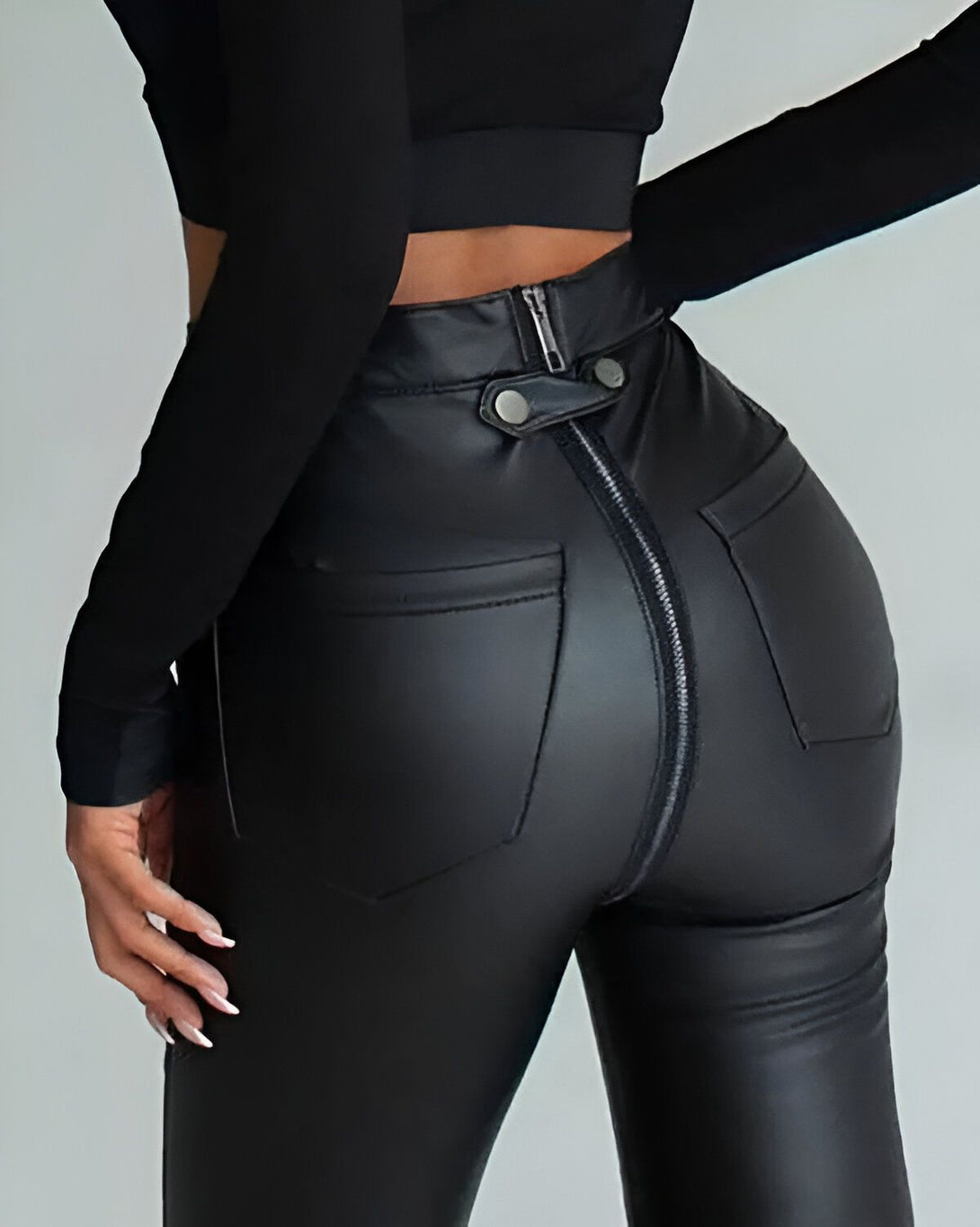 Une femme porte un pantalon en cuir noir avec une fermeture éclair au dos.