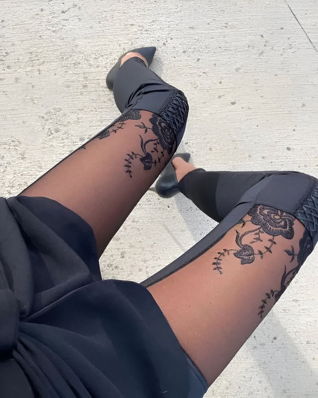 Une femme porte des collants noirs transparents avec des motifs floraux et des talons aiguilles noirs.