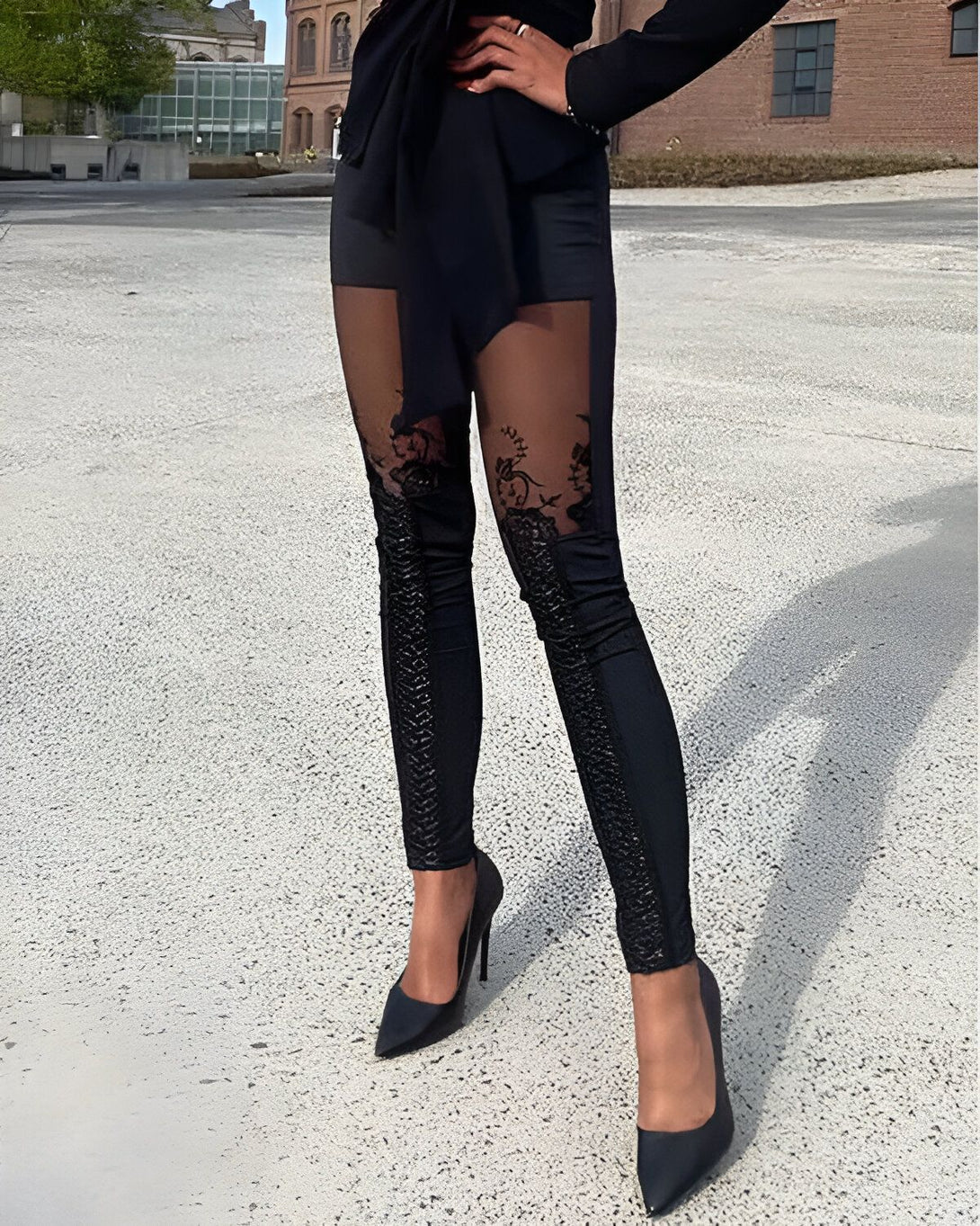 Une femme porte un legging noir avec des empiècements en dentelle, un chemisier noir et des escarpins noirs.