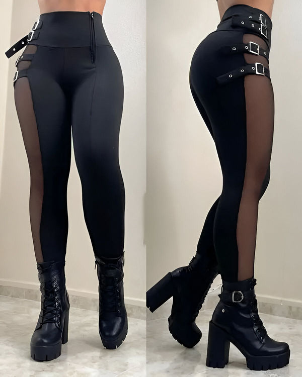 Une femme porte un legging noir avec des découpes sur les côtés et des boucles. Elle porte également des bottes noires à talons hauts.