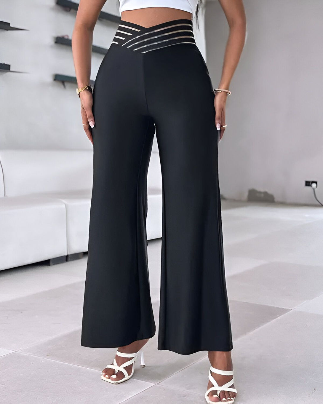 Une femme porte un pantalon taille haute noir avec des talons blancs.
