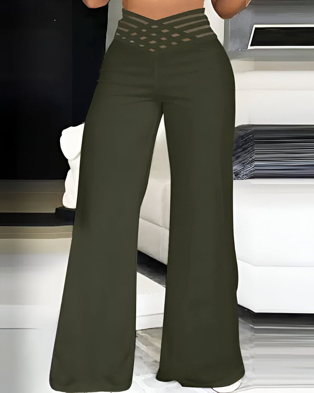 Une femme porte un pantalon taille haute vert olive. Le pantalon est évasé et a une coupe ample. La femme est debout dans une pièce, adossée à un mur.