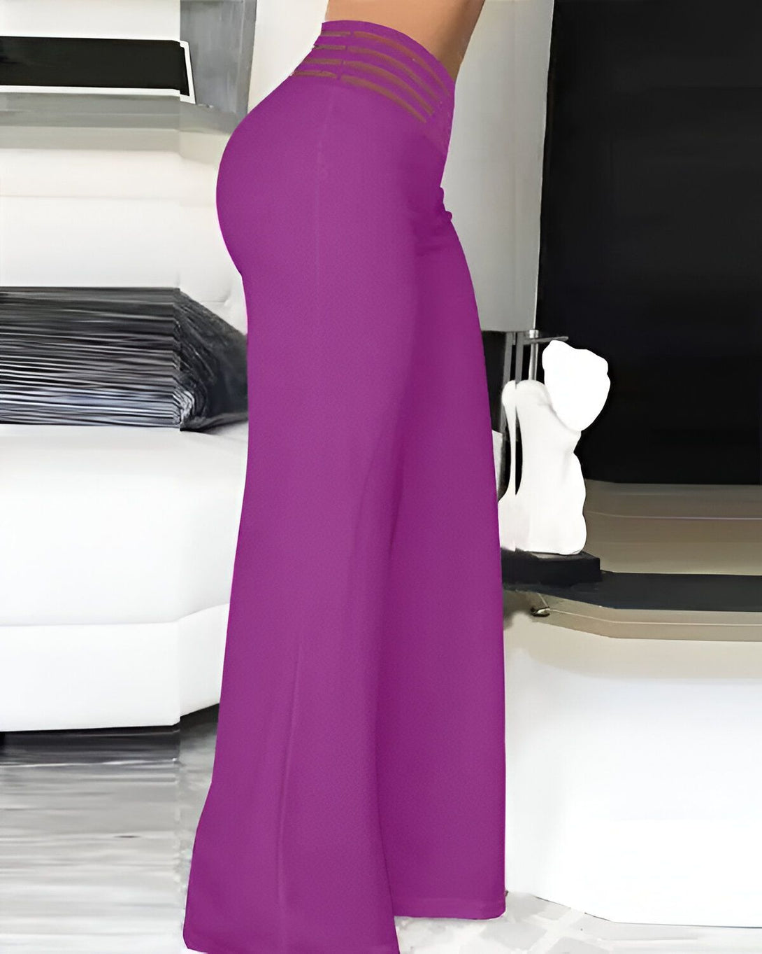 Une femme porte un pantalon large et évasé de couleur fuchsia. Le pantalon est taille haute et possède une ceinture à nouer. La femme est vue de dos et porte des talons hauts.