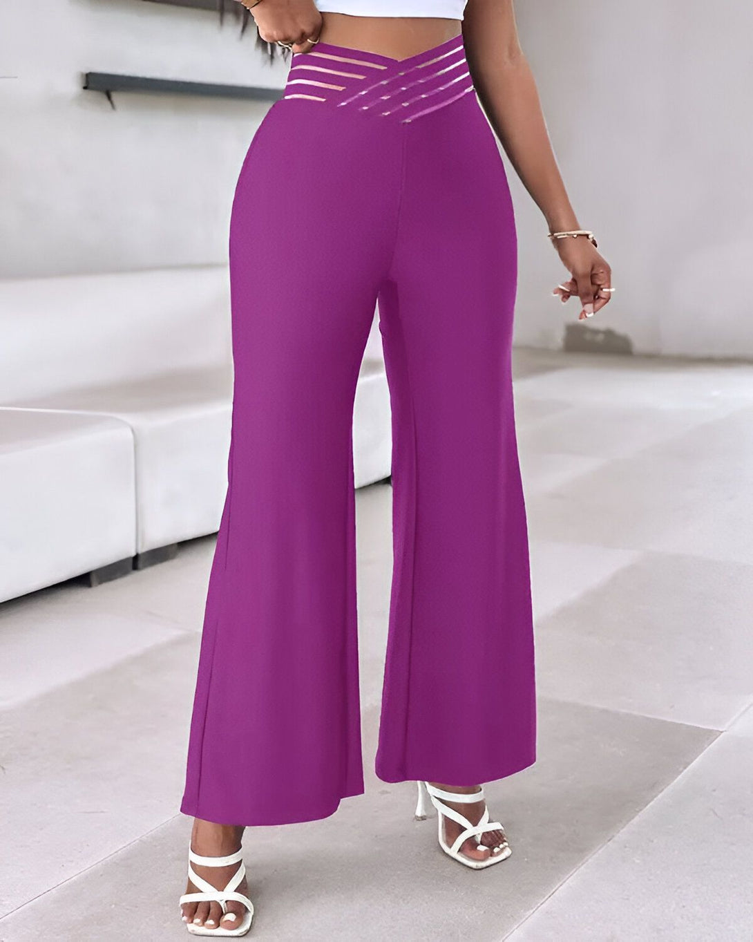 Une femme porte un pantalon large violet taille haute avec des talons blancs.