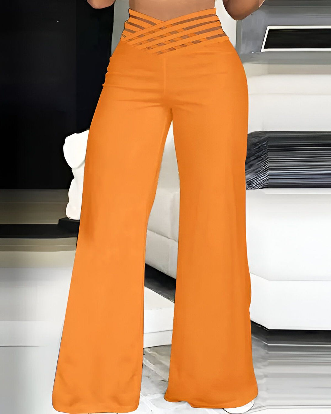 Une femme porte un pantalon orange taille haute avec une ceinture croisée. Le pantalon est ample et évasé.