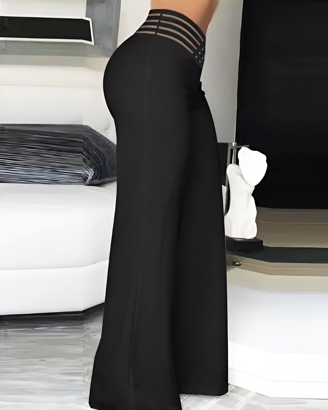 Une femme porte un pantalon large noir taille haute avec une ceinture à lacets. Elle est vue de côté et porte des talons hauts noirs.