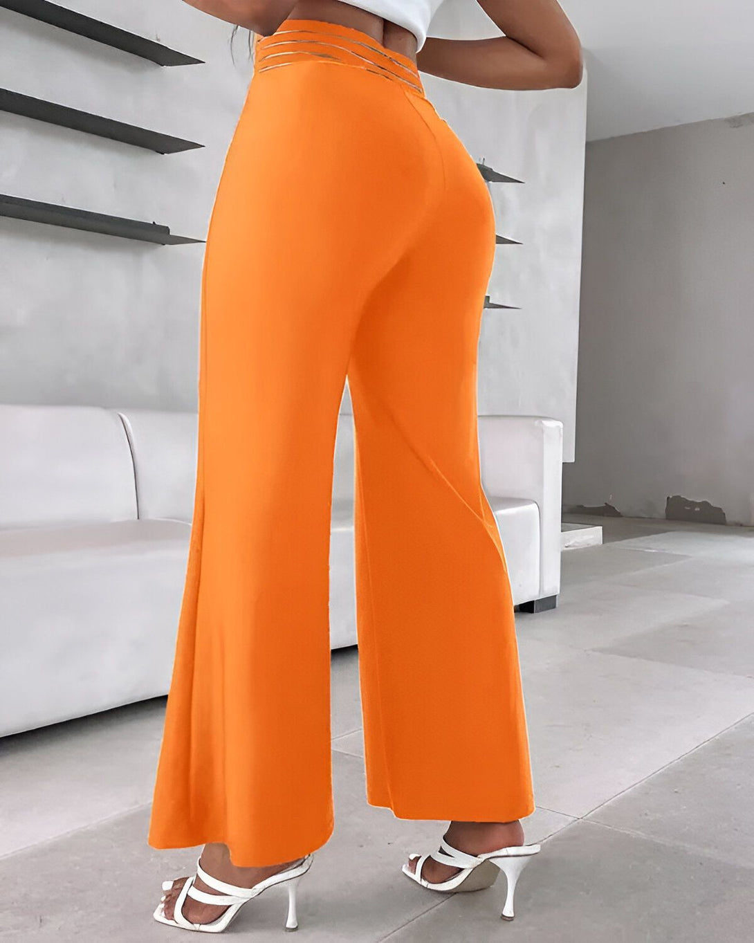 Une femme porte un pantalon orange taille haute et évasé. Elle est vue de dos.