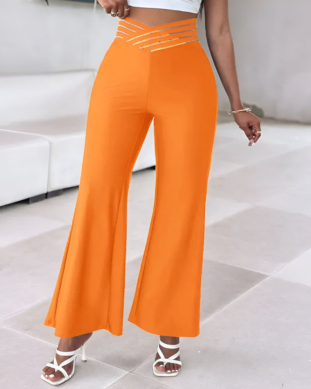 Une femme porte un pantalon orange taille haute évasé avec des talons blancs.