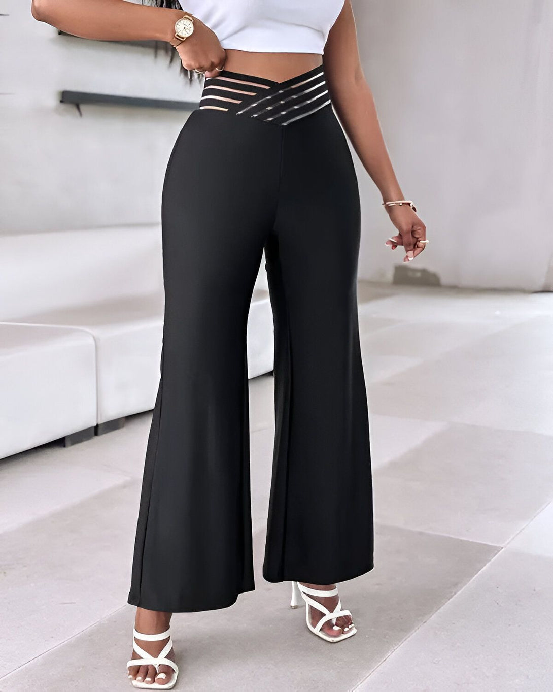 Une femme porte un pantalon taille haute noir avec une ceinture à lacets. Elle porte également un haut blanc et des sandales à talons blancs.