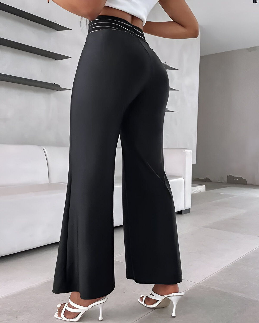 Une femme porte un pantalon noir taille haute évasé avec une ceinture blanche. Elle est vue de dos et porte des sandales à talons blancs.