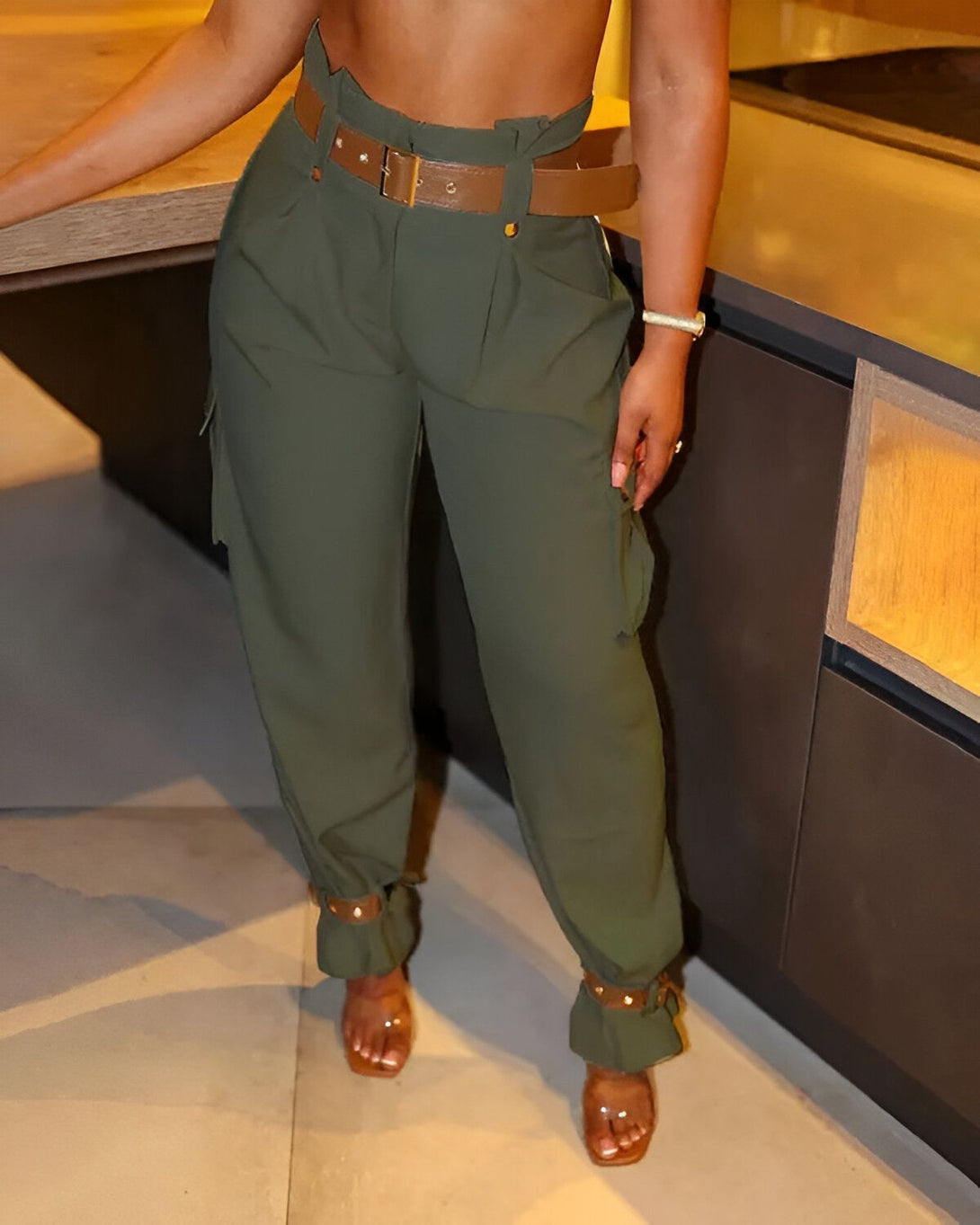 Une femme porte un pantalon cargo vert olive taille haute avec une ceinture marron. Elle est également pieds nus.