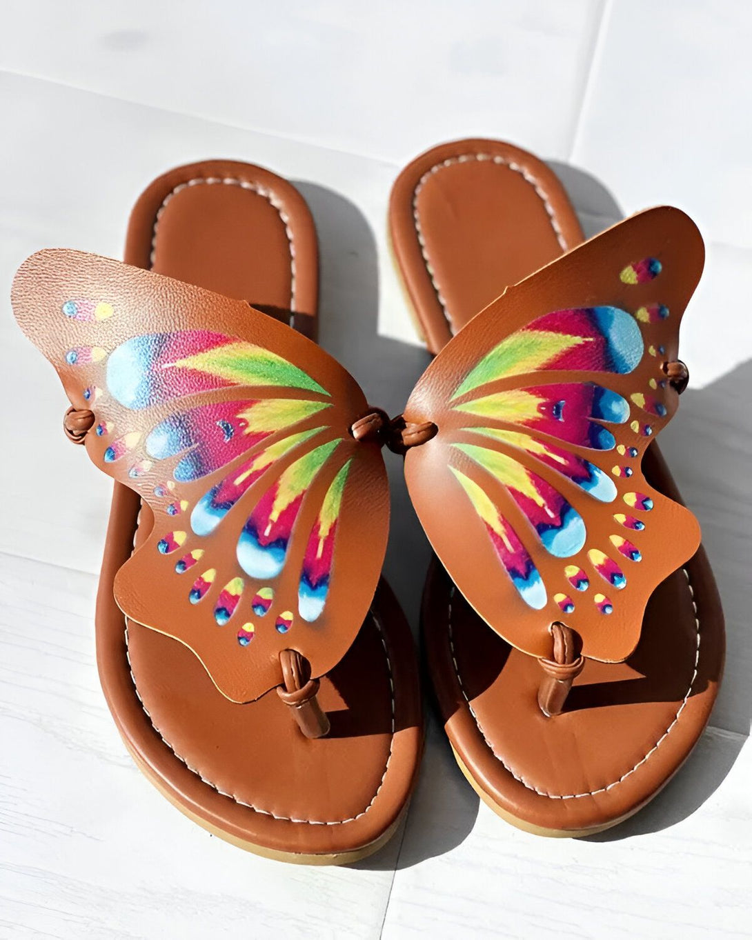 Une paire de tongs marron avec un motif papillon coloré sur le dessus.