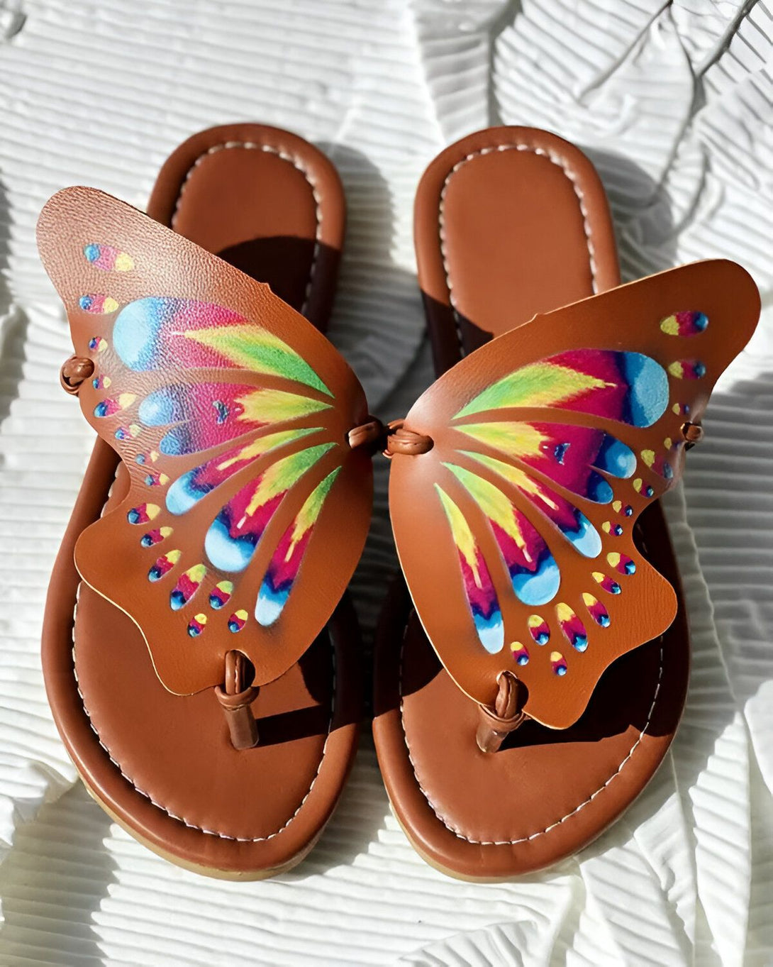 Une paire de tongs marron avec des ailes de papillon arc-en-ciel.
