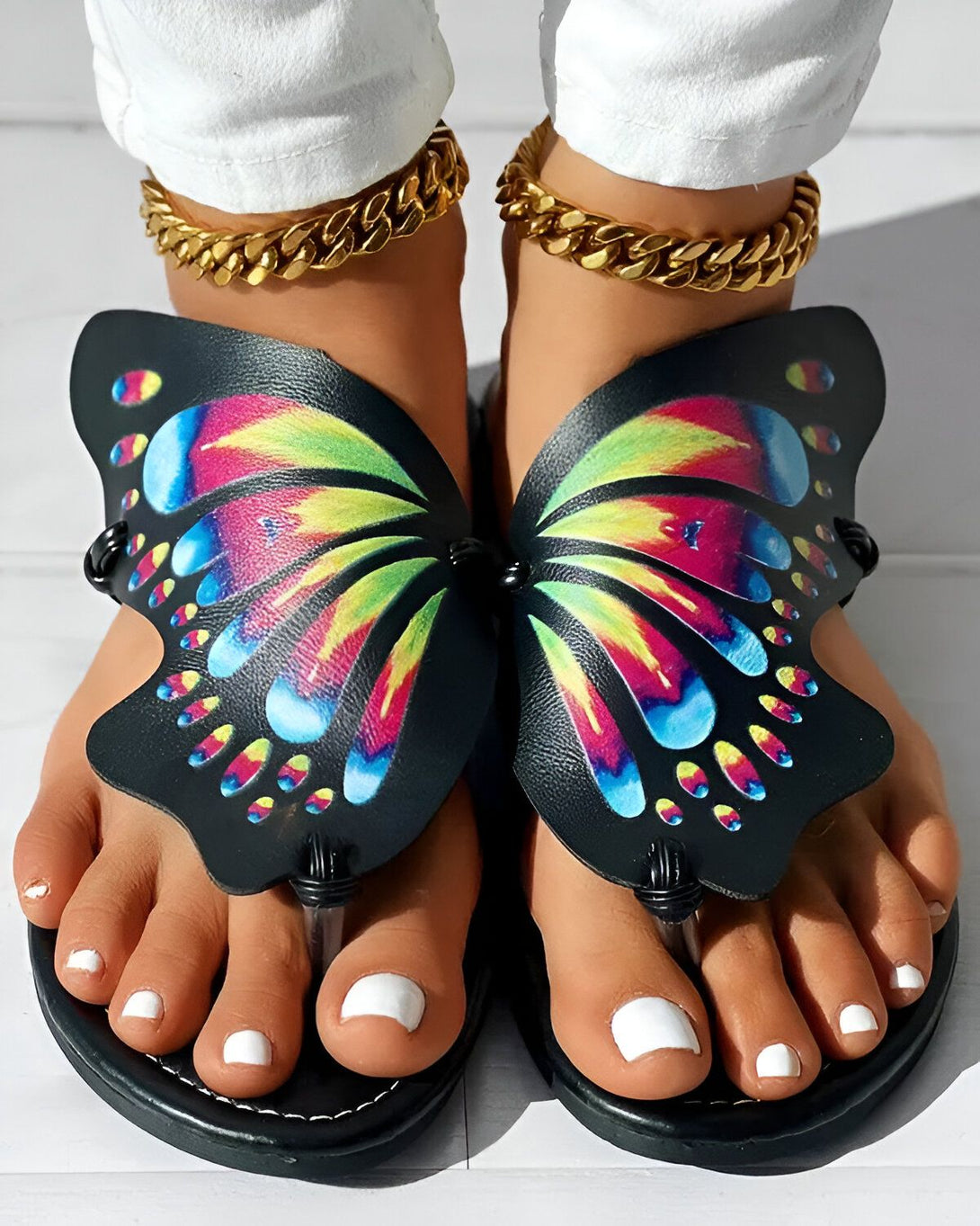 Une femme porte des sandales noires en forme de papillon. Les ailes du papillon sont colorées et ont des motifs de fleurs.