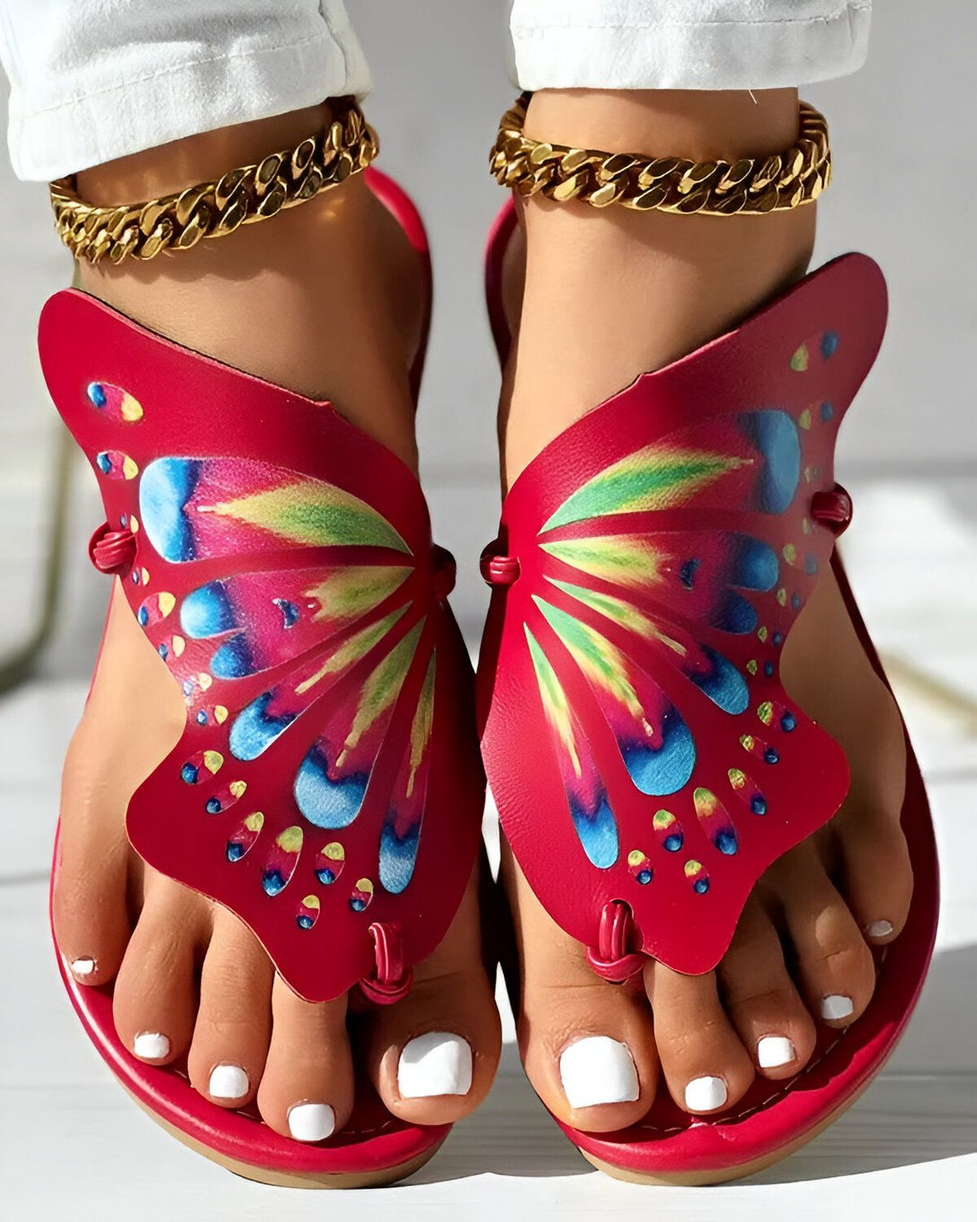 Une paire de sandales rouges en forme de papillon avec des motifs multicolores sur le dessus et des brides dorées autour de la cheville.