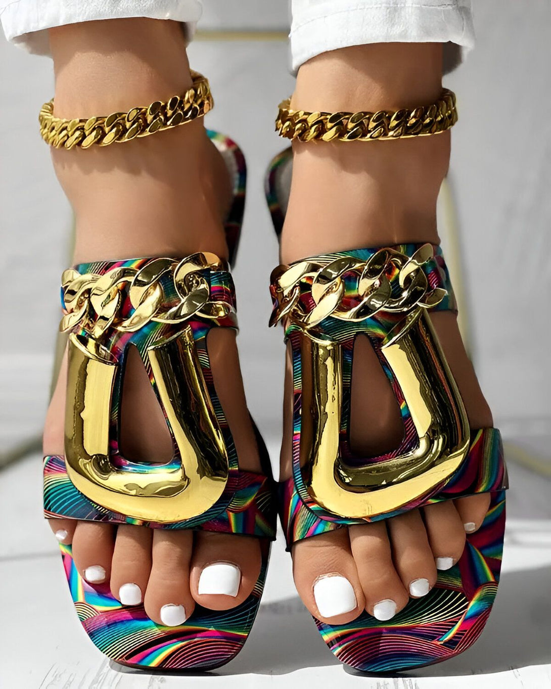Une femme porte des sandales à talons hauts multicolores avec des chaînes dorées sur le dessus.