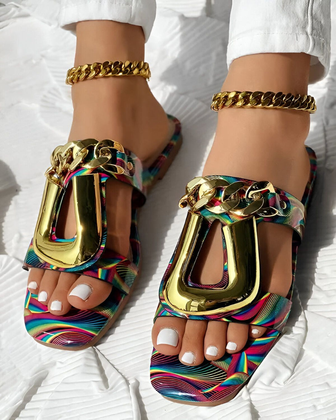 Une femme porte des sandales multicolores à talons hauts avec des chaînes dorées.
