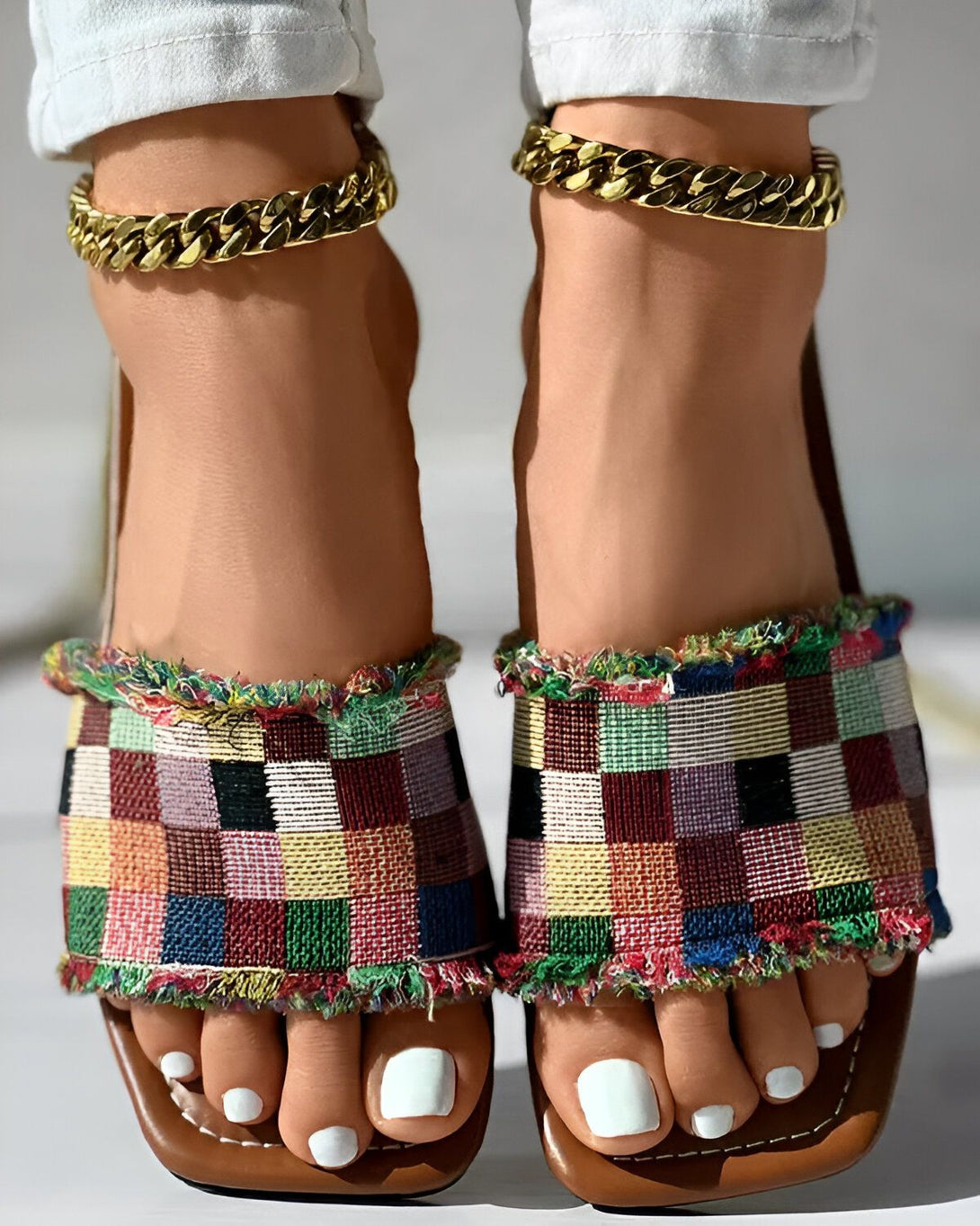 Une image de pieds avec des sandales colorées à talons et des chaînes dorées aux chevilles.