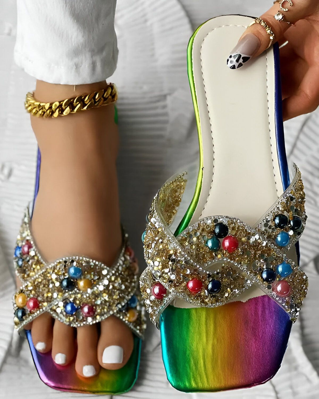 Une femme porte des sandales plates arc-en-ciel avec des brides croisées et des perles colorées.
