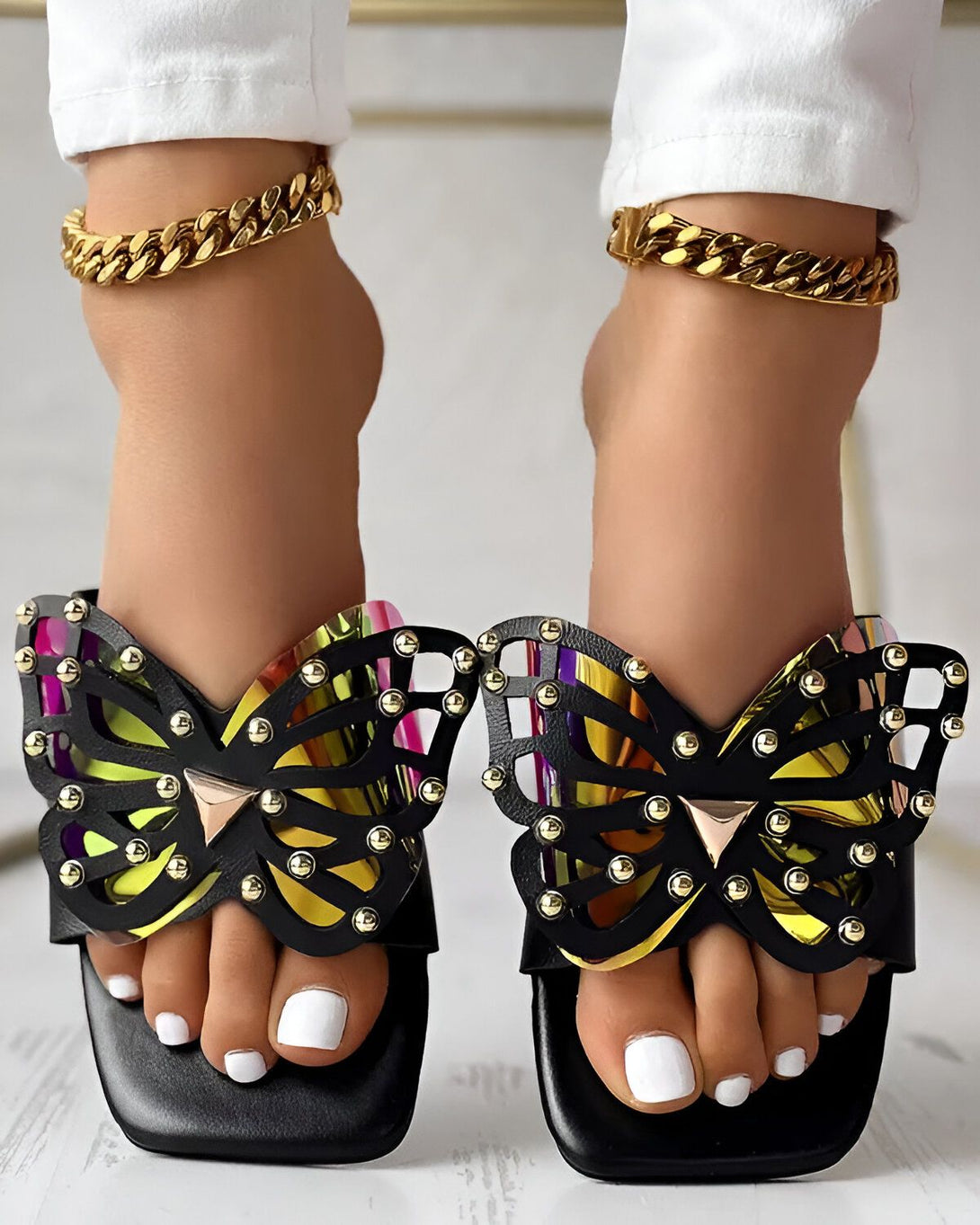 Une femme porte des sandales noires à talons hauts avec des ailes de papillon dorées.