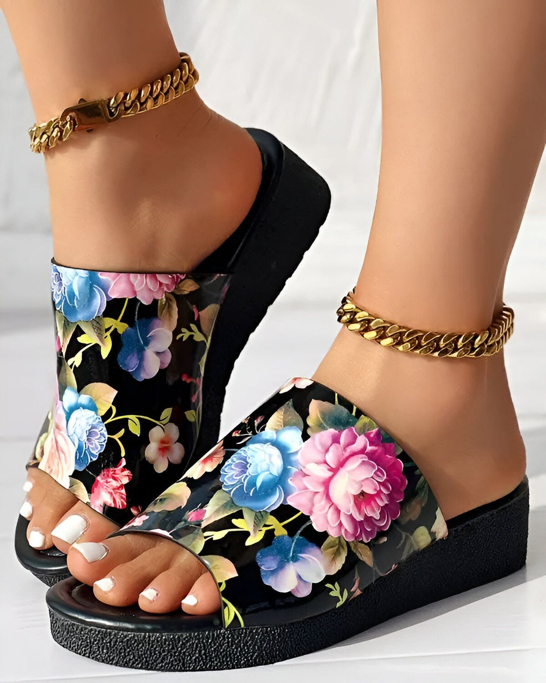 Une femme porte des sandales à plateforme noires à motif floral. Les sandales sont ornées d'une chaîne dorée.