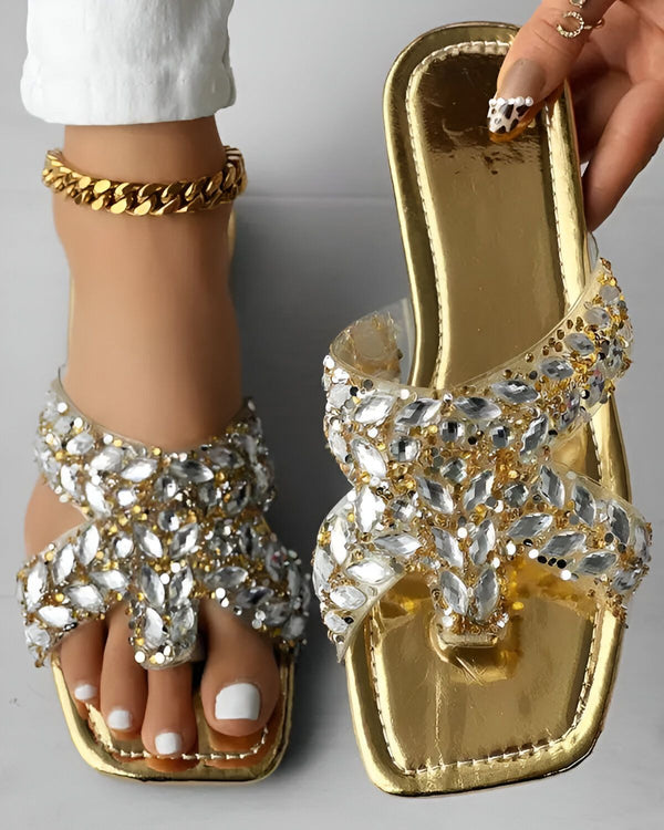 Une paire de sandales dorées à talons hauts avec des brides transparentes et des strass.