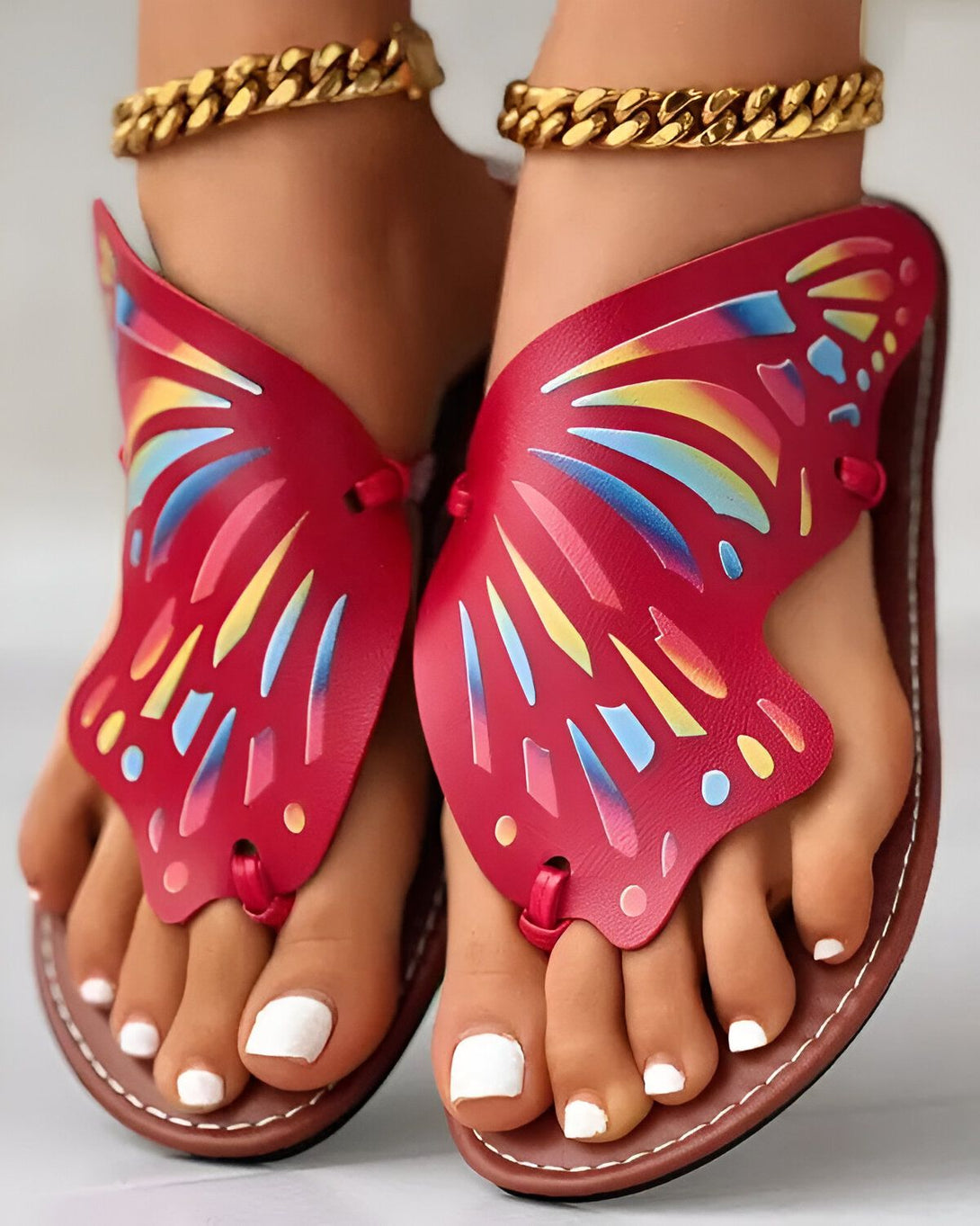 Une paire de sandales rouges en forme de papillon avec des lanières dorées.