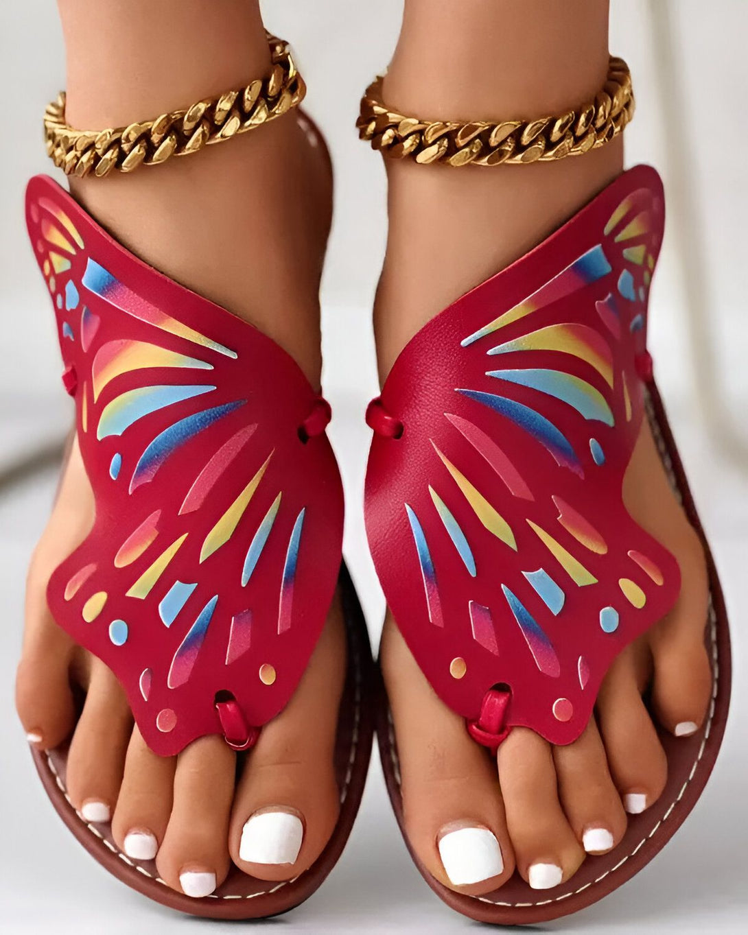 Une paire de sandales rouges en forme de papillon avec des lanières dorées.