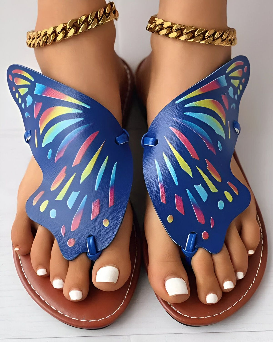 Une paire de sandales plates bleues en forme de papillon avec des lanières dorées autour des chevilles.