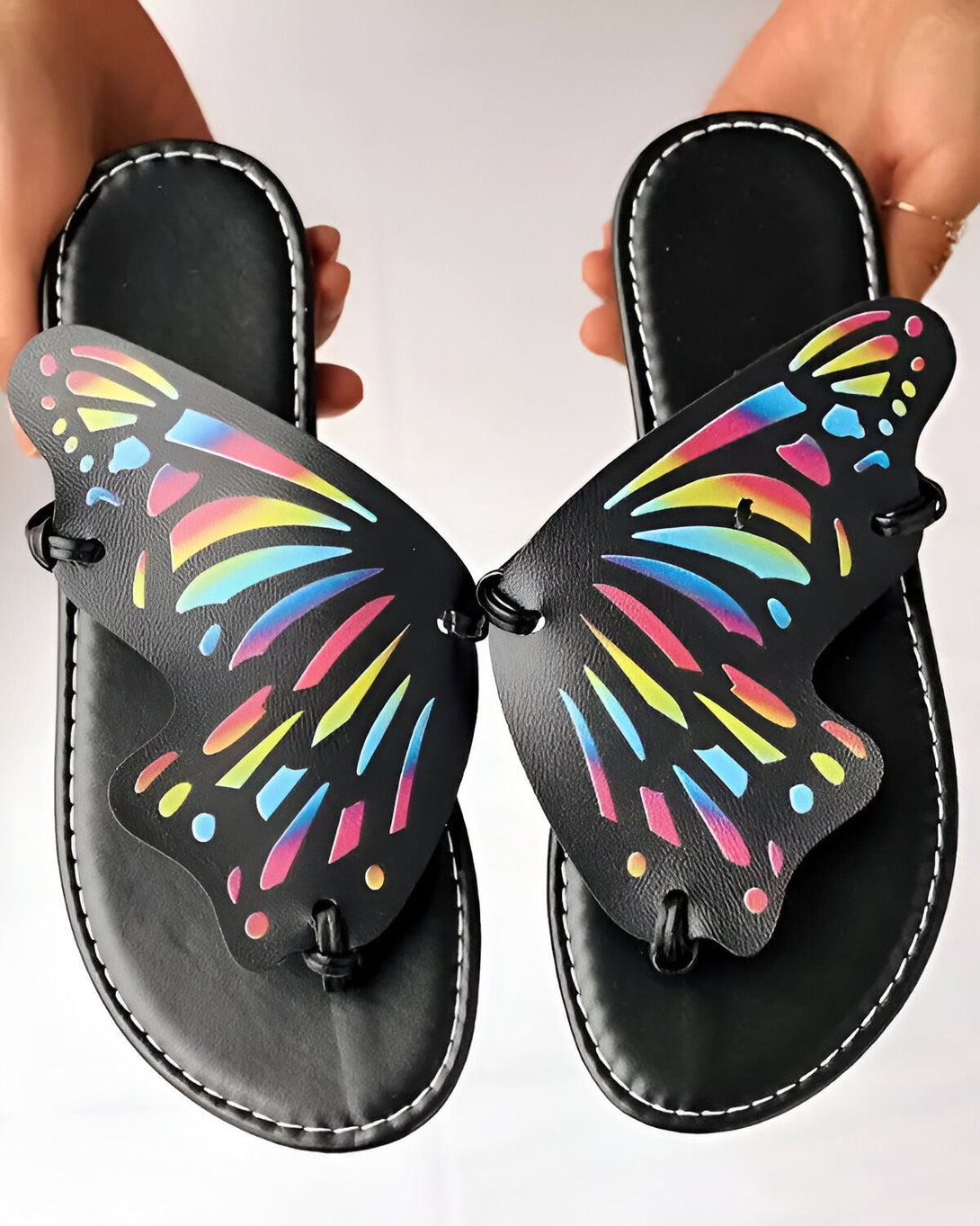 Une paire de tongs noires en forme de papillon avec un motif arc-en-ciel sur les ailes.