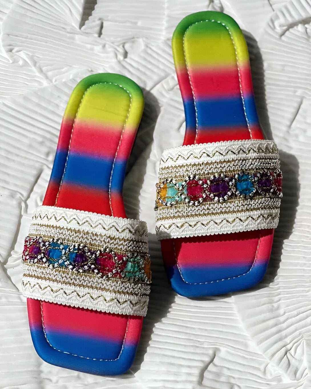 Une paire de sandales plates arc-en-ciel avec des perles et des broderies colorées.