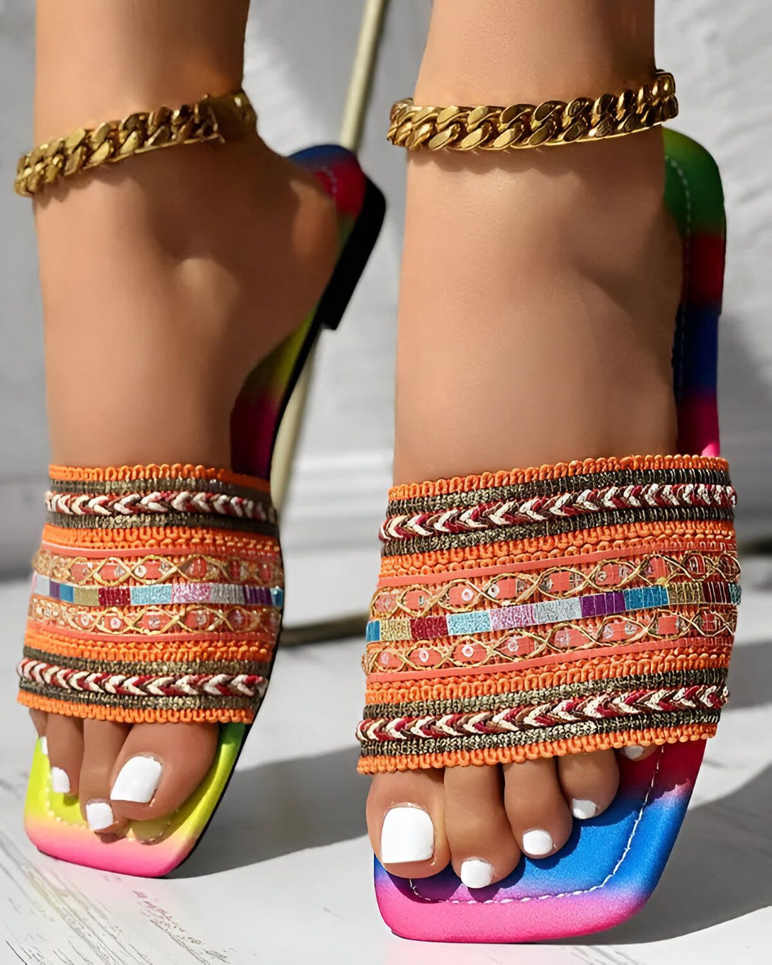 Une femme porte des sandales plates multicolores avec des motifs ethniques et des brides dorées.