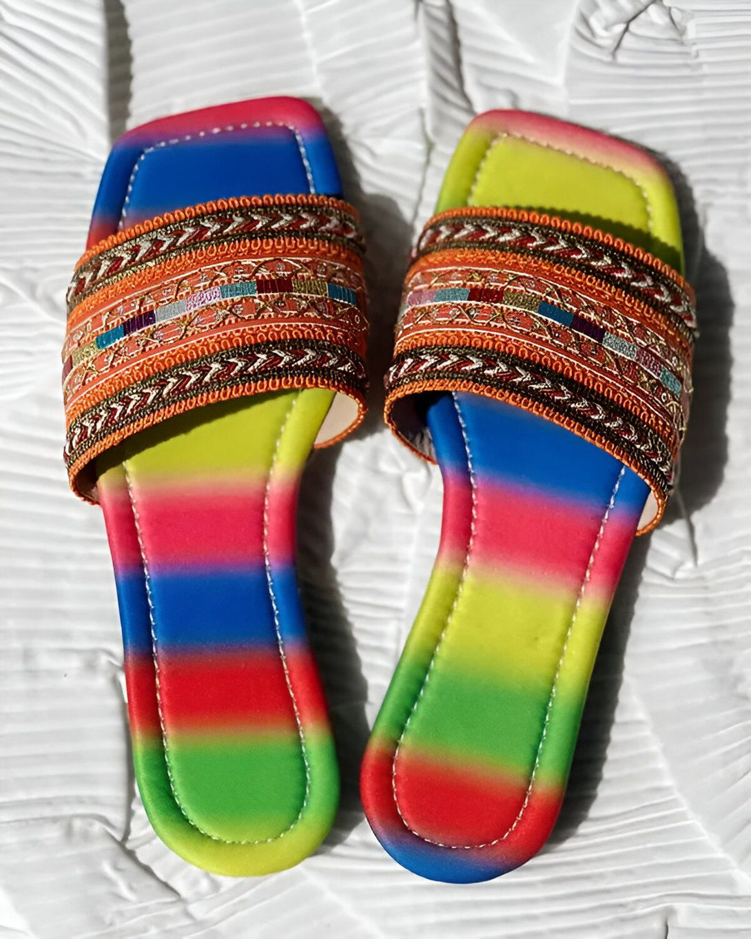 Une paire de sandales plates arc-en-ciel avec des broderies colorées sur le dessus.