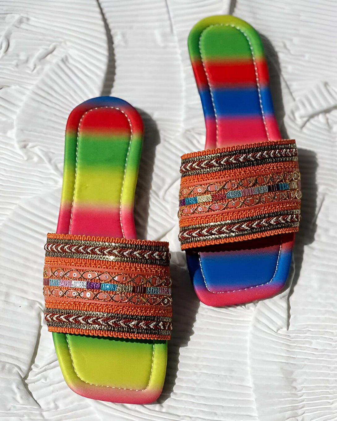Une paire de sandales plates arc-en-ciel avec des broderies colorées.