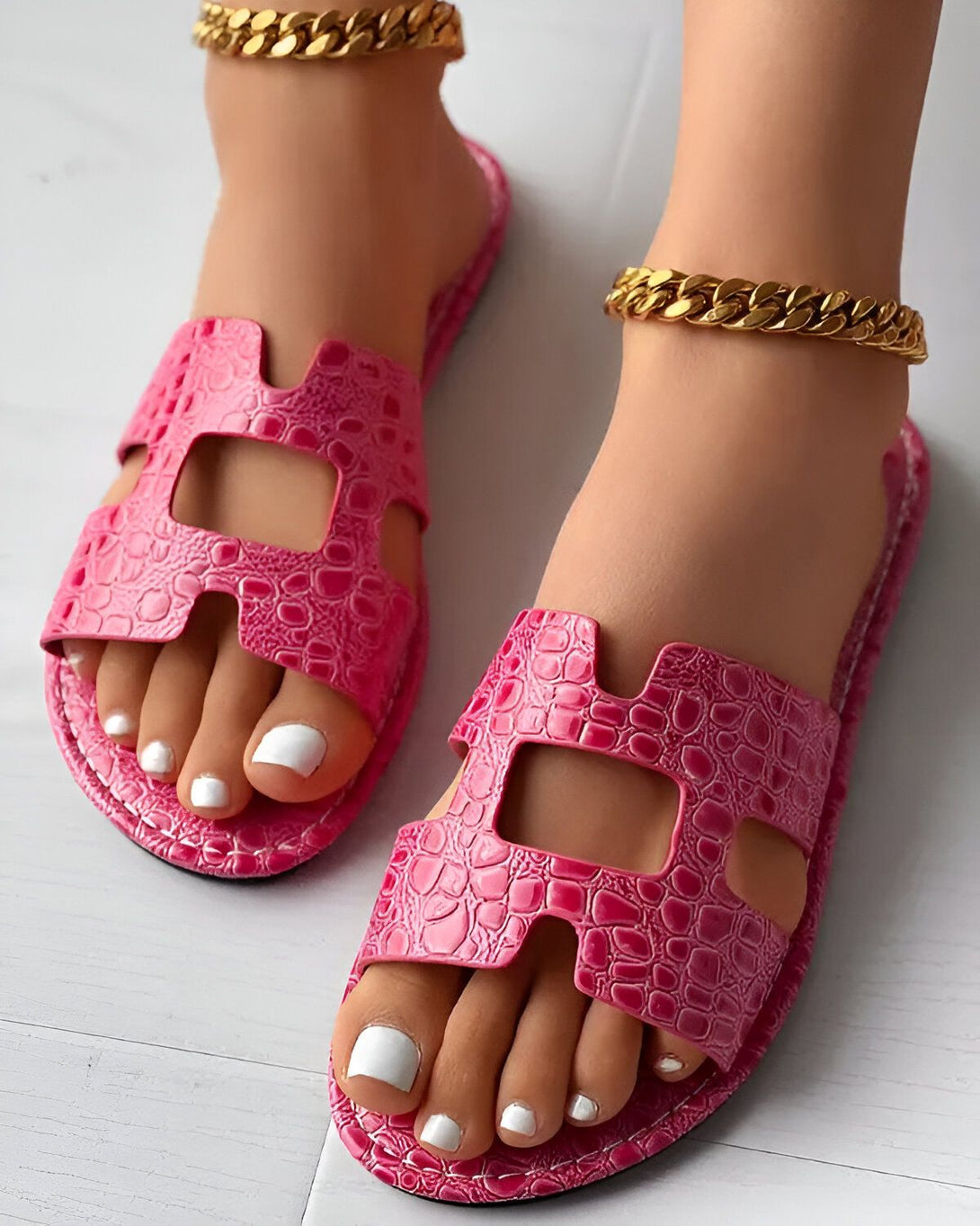 Une paire de sandales roses en cuir avec une chaîne dorée sur le pied gauche.