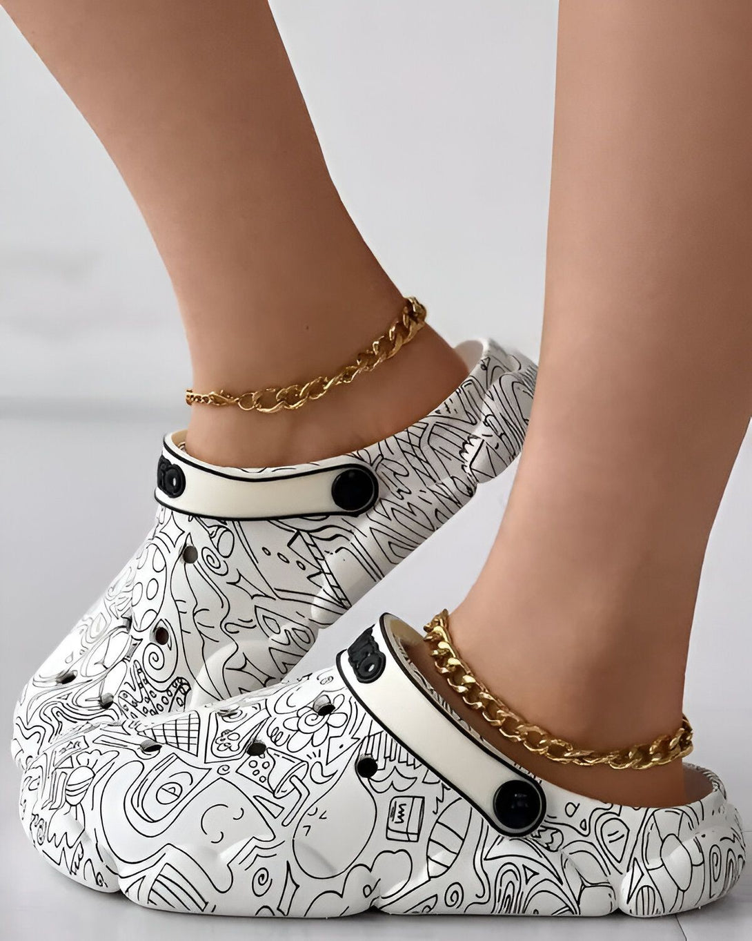 Une paire de sabots blancs avec des motifs noirs et des chaînes dorées.