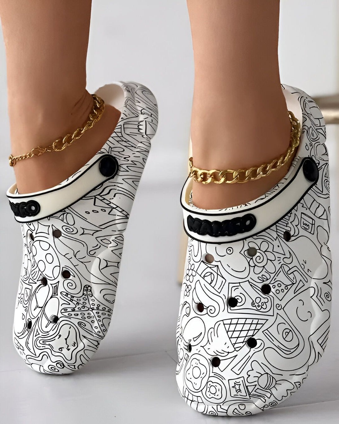 Une paire de sabots blancs avec des motifs noirs et une chaîne en or.