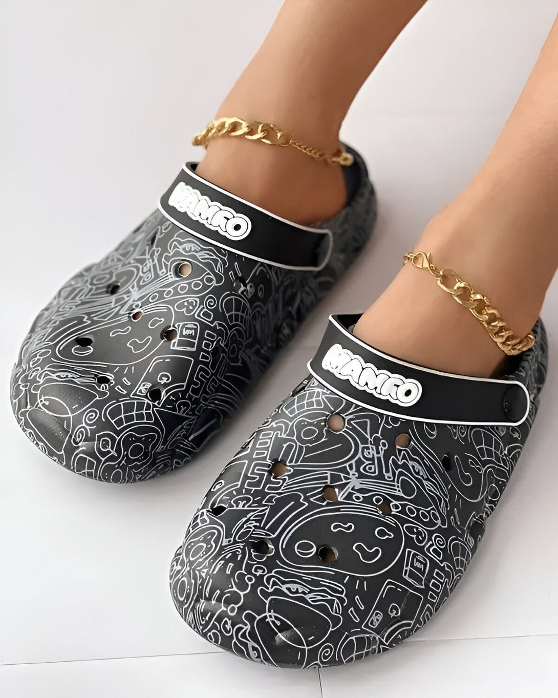 Une paire de sabots noirs et blancs avec des motifs de dessins animés. Les sabots sont portés par une personne qui porte également des chaussettes blanches et un pantalon noir.